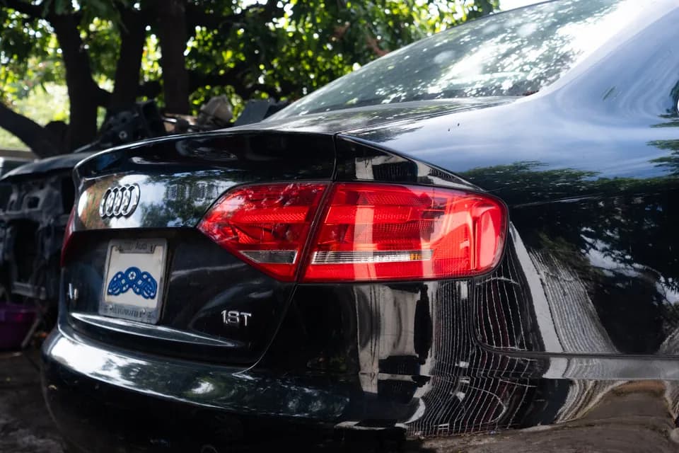 Audi rear badge and red tail lamp reflecting trees in the workshop yard