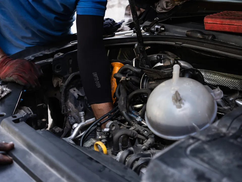 A technician’s gloved hands at work between engine components and the coolant reservoir