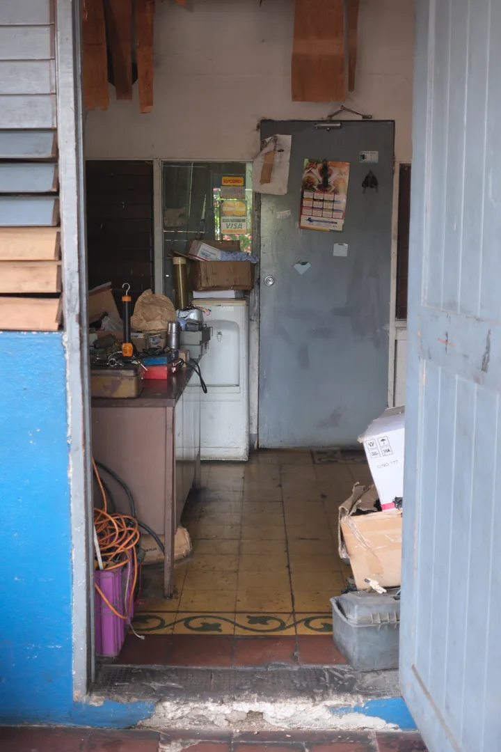 A view through the open workshop office doorway, with blue walls, tools and worn floor tiles