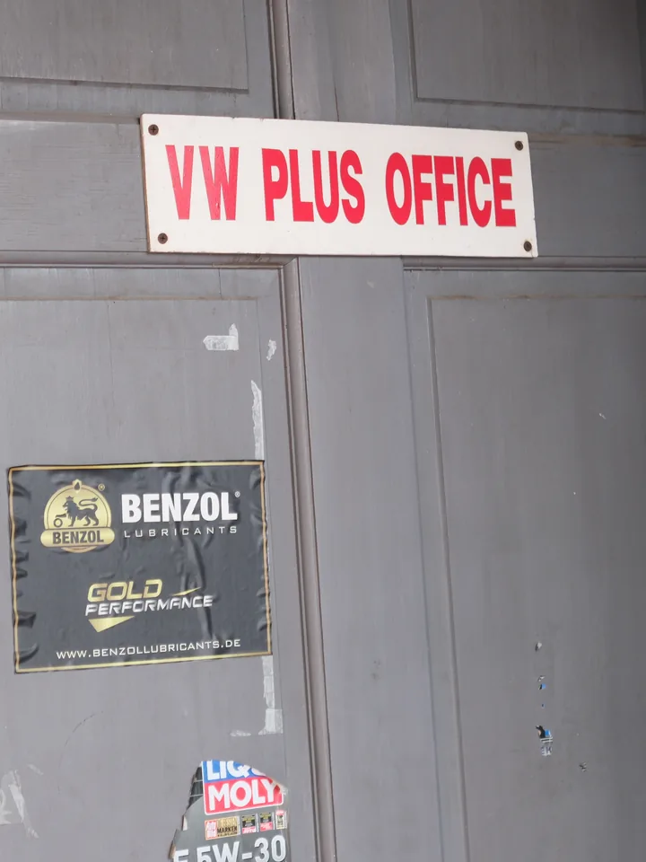 The red VW PLUS office sign on a weathered grey door