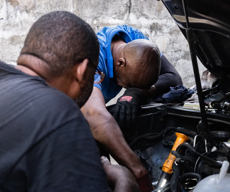 Two technicians leaning into an open engine bay, working together with hand tools